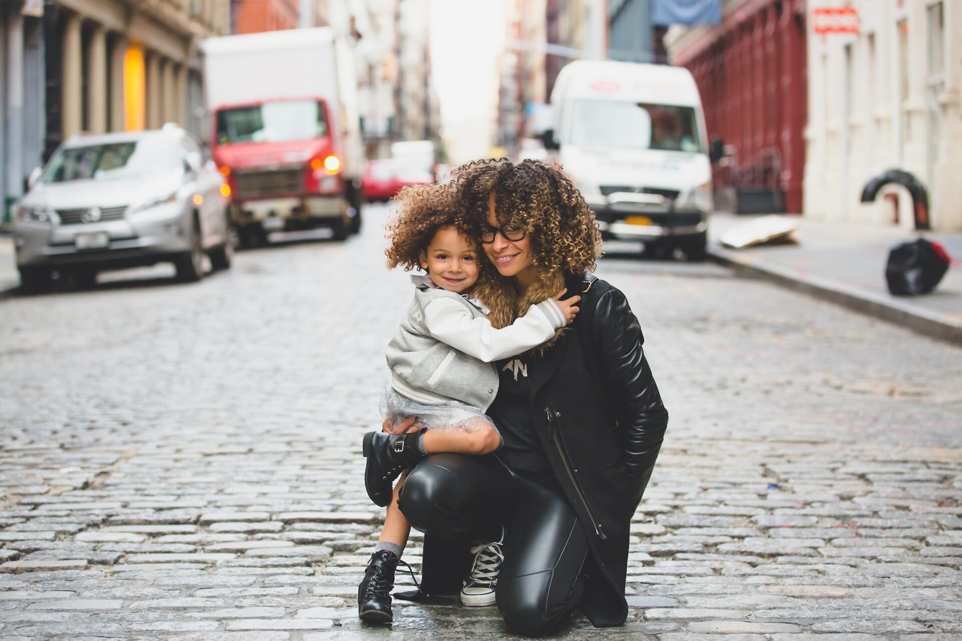 Happy young mom is hugging her cute little daughter on the street